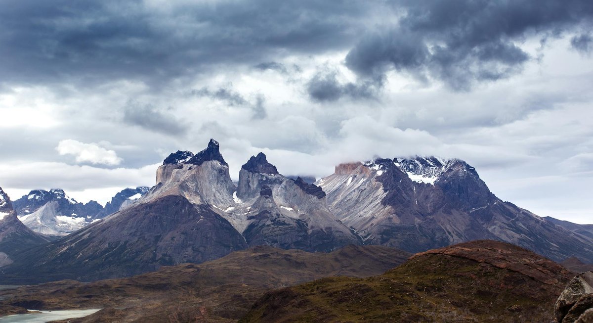 Dramatic mountain peaks of Torres del Paine with moody clouds and golden light on wild Patagonian grassland