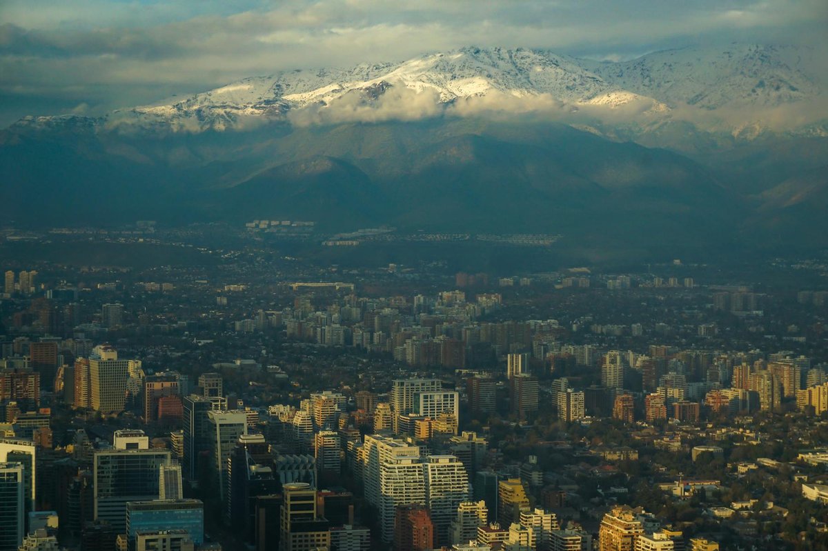 Aerial view of Santiago Chile cityscape with snow-capped Andes mountains rising behind the urban sprawl at sunset