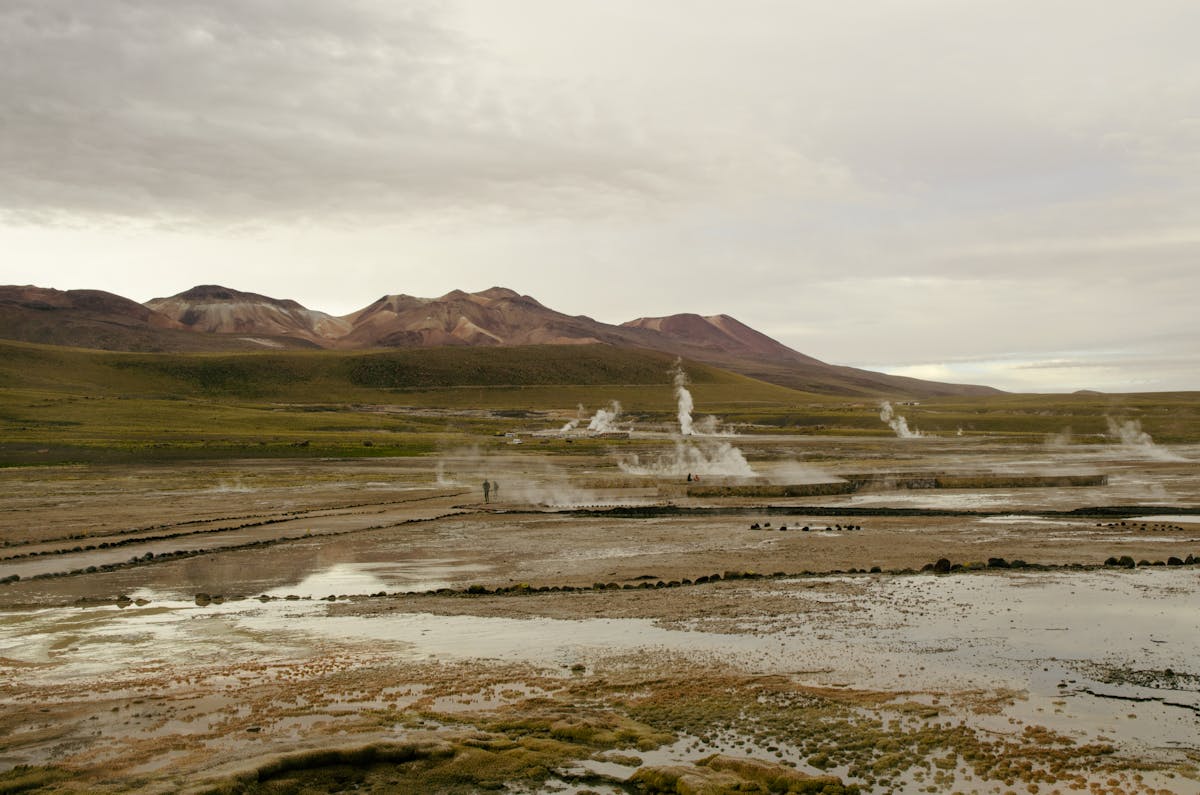Steam rising dramatically from geysers across a barren landscape with distant mountains