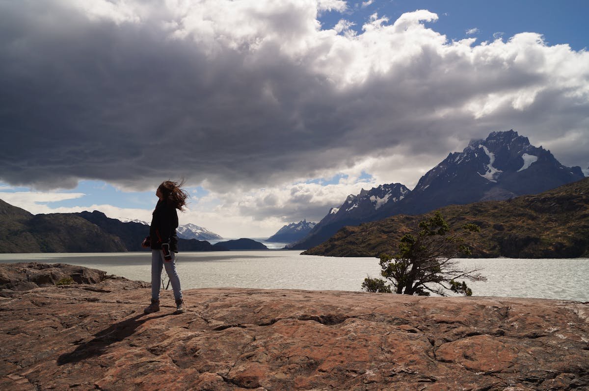 A traveler standing on a rock overlooking Torres del Paine mountains with dramatic clouds