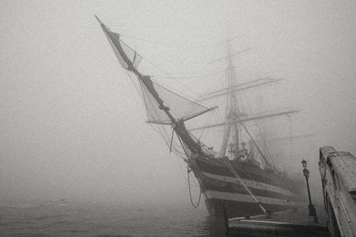 A historic sailing ship docked in a foggy harbour in black and white