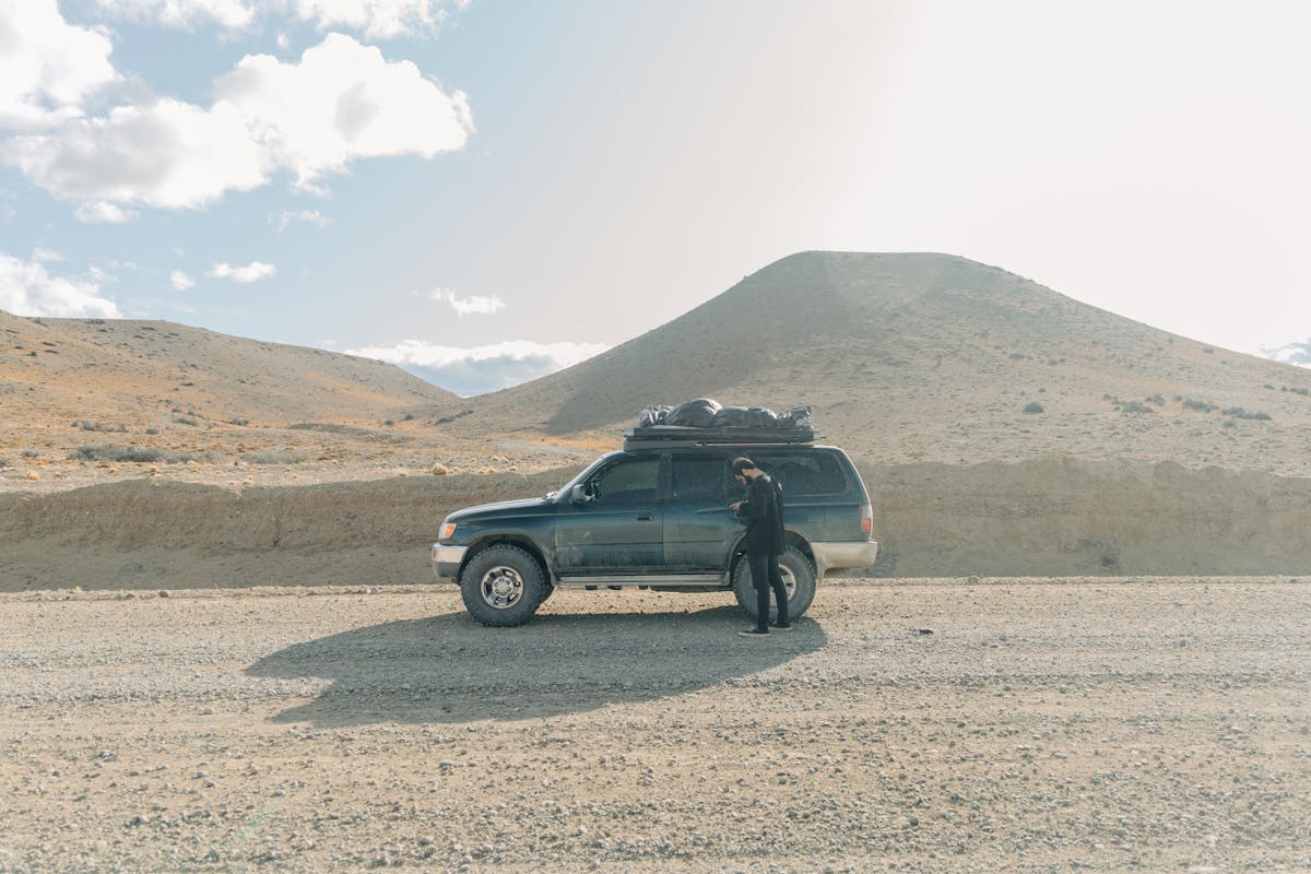 Man standing beside an SUV on a gravel road in a desert-like Patagonian landscape