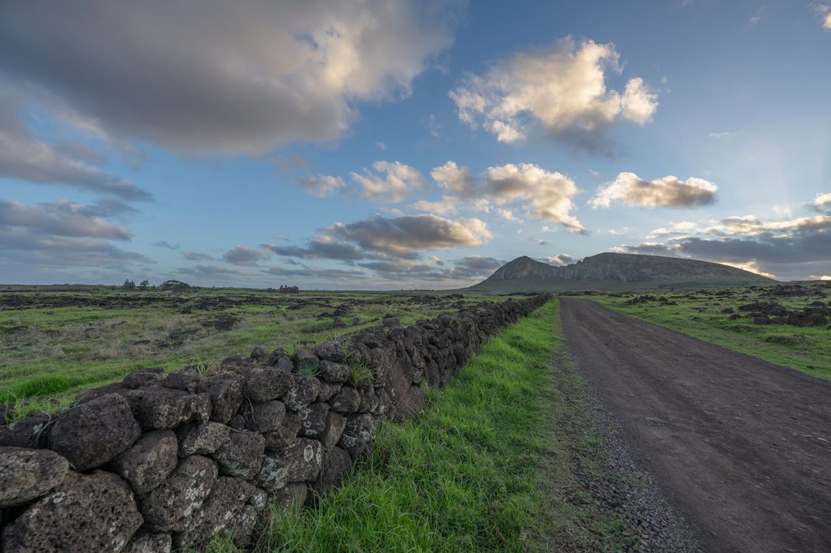 Green landscape and stone walls near Rano Raraku on Easter Island with dramatic sky