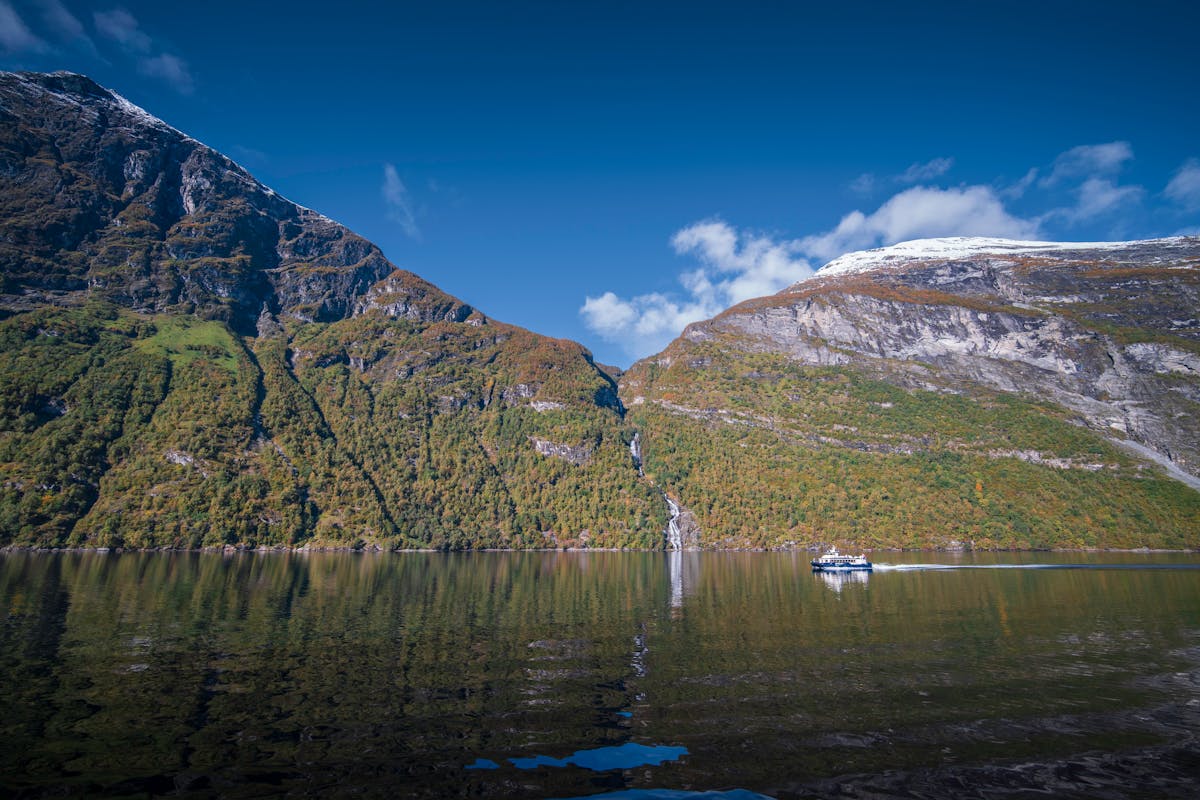 Ferry crossing through a fjord with snow-capped mountains reflecting on calm waters