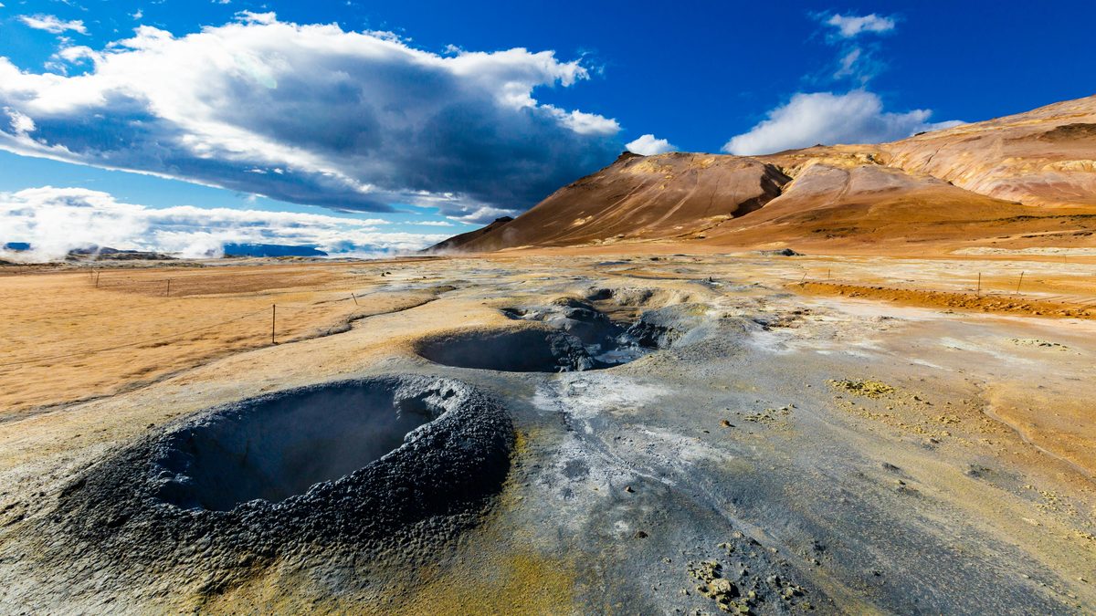 Geothermal landscape with steam rising from desert terrain and volcanic hills