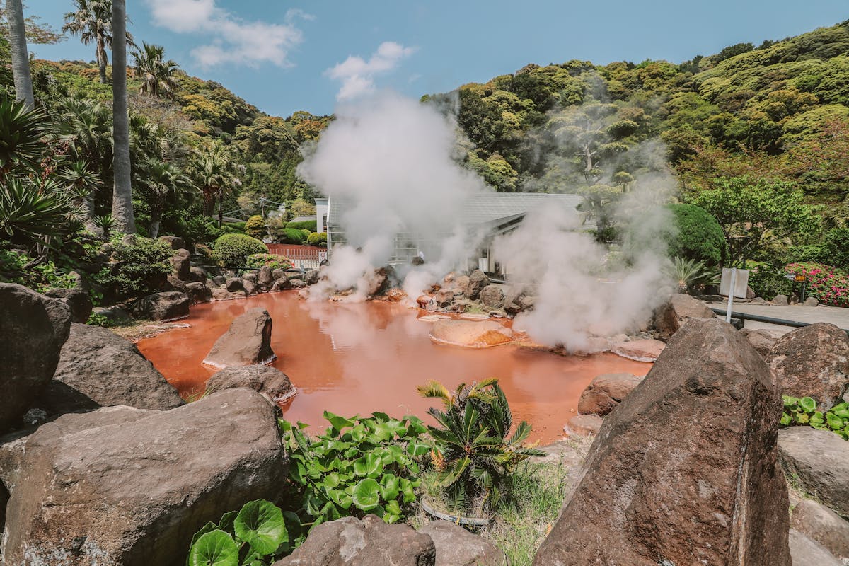 Natural hot spring pool surrounded by lush green vegetation with steam rising