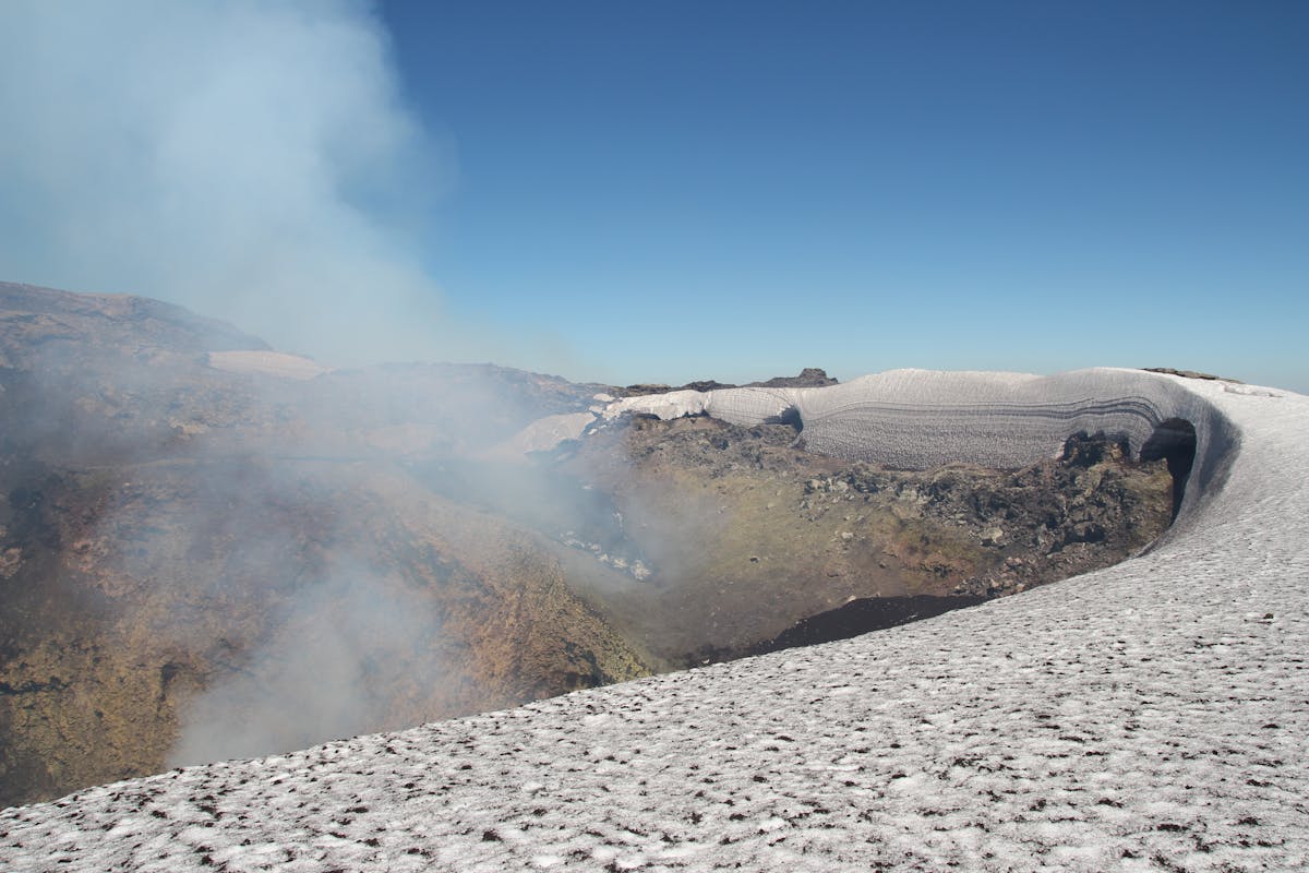 Snow-covered crater of Villarrica Volcano with steam rising under clear blue skies