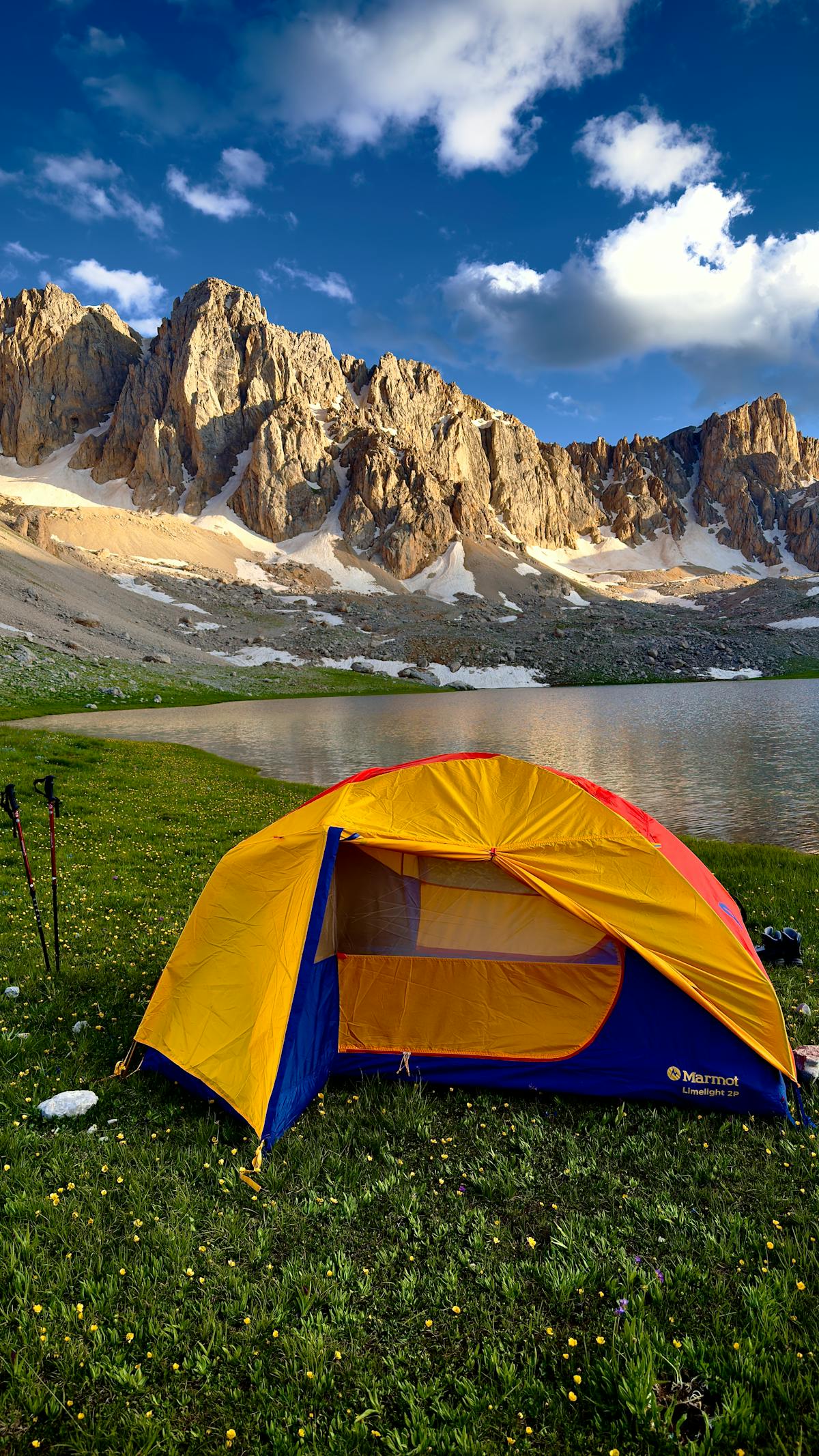 Camping tent pitched beside a serene mountain lake with peaks at sunset