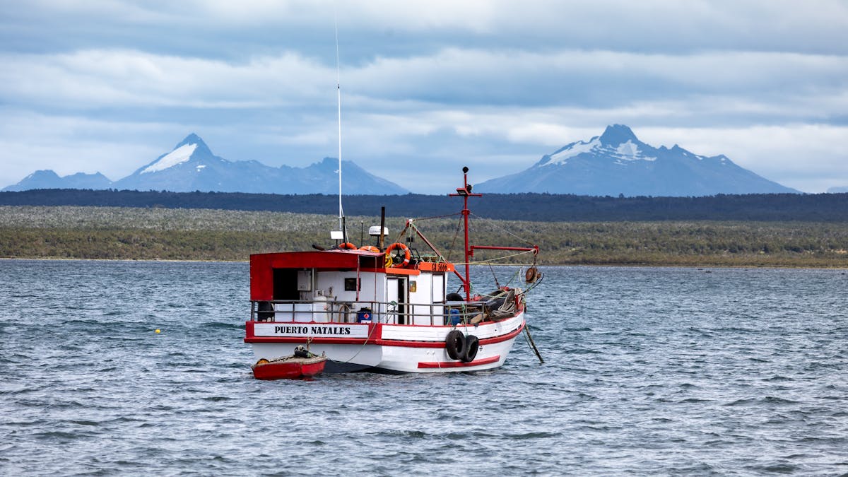 Wooden fishing boat on calm water with mountains behind in Puerto Natales Chile