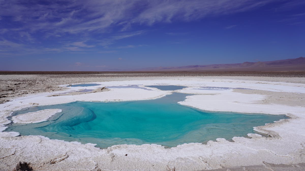 Turquoise salt lagoon in the Atacama Desert surrounded by white mineral-crusted shore