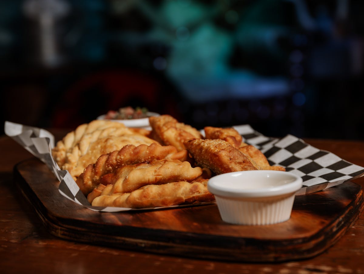 Fried empanadas arranged on a wooden tray with dipping sauce
